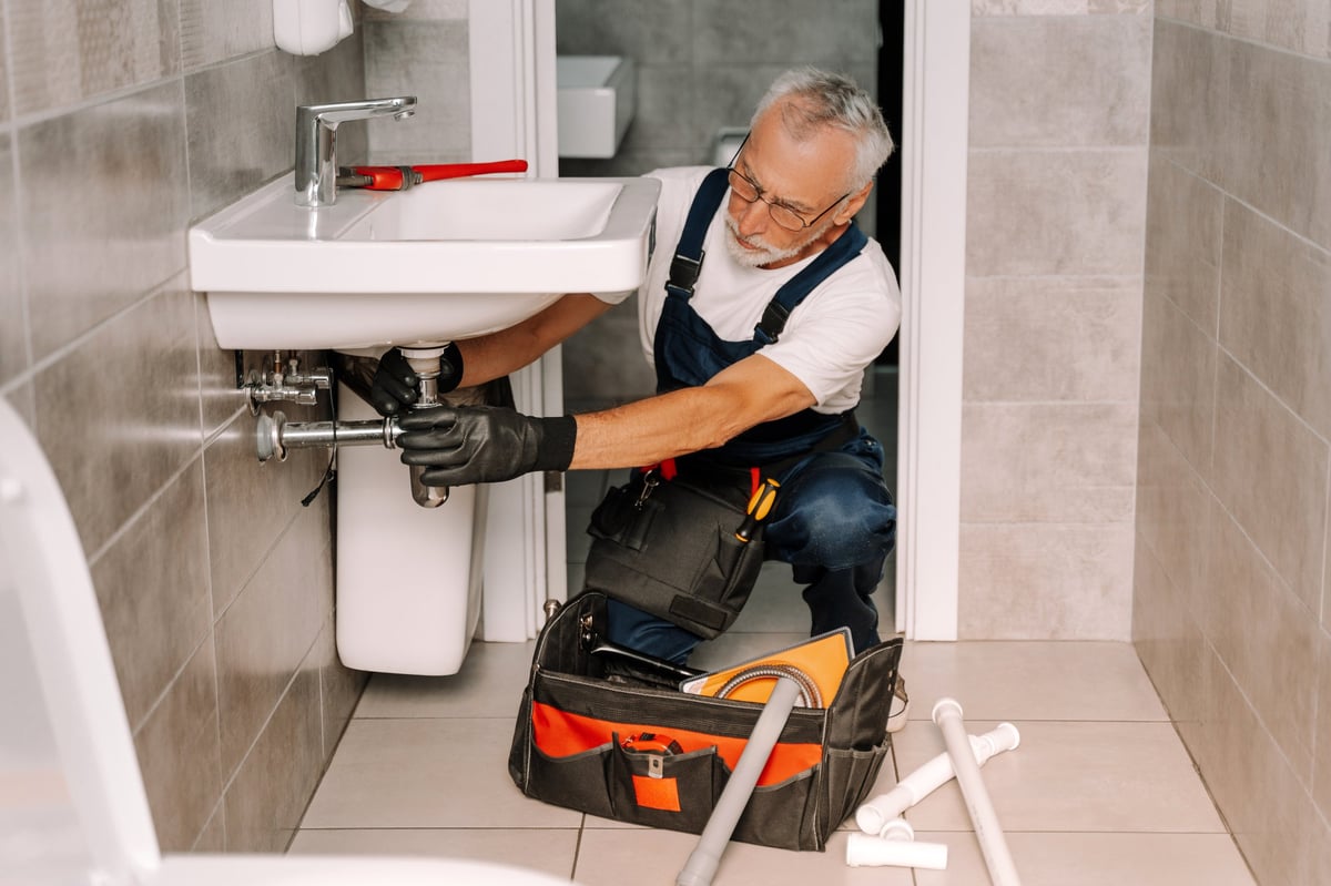 Plumber working under a sink with a wrench installing piping