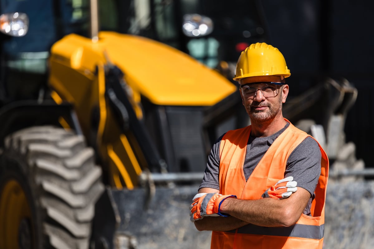 A construction worker wearing an orange vest and hard hat at a construction site, representing skilled trades professionals
