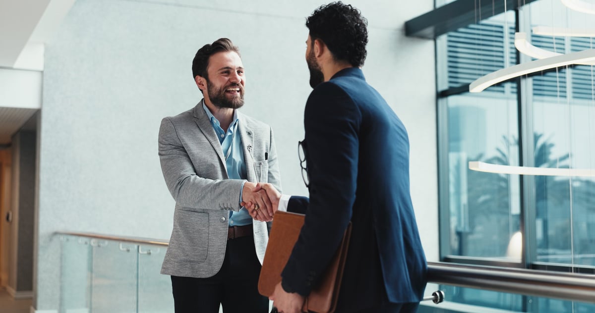 Two professionals shaking hands by a window during a partnership meeting in a modern office