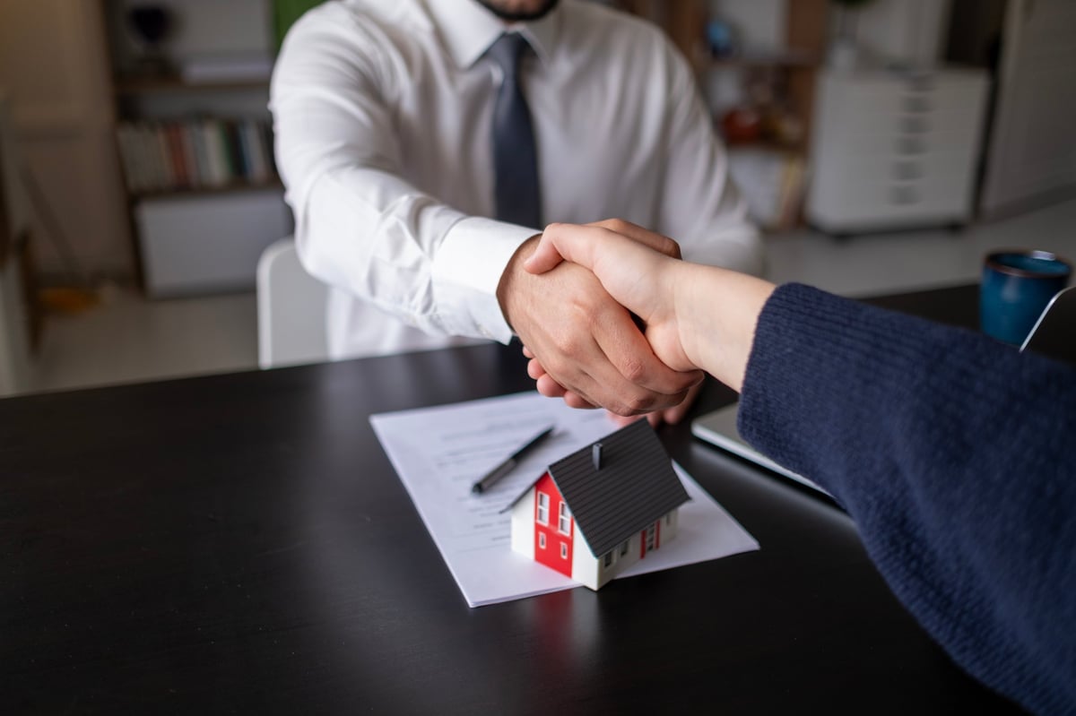 Real estate agent holding keys and a for-sale sign outside a newly listed home