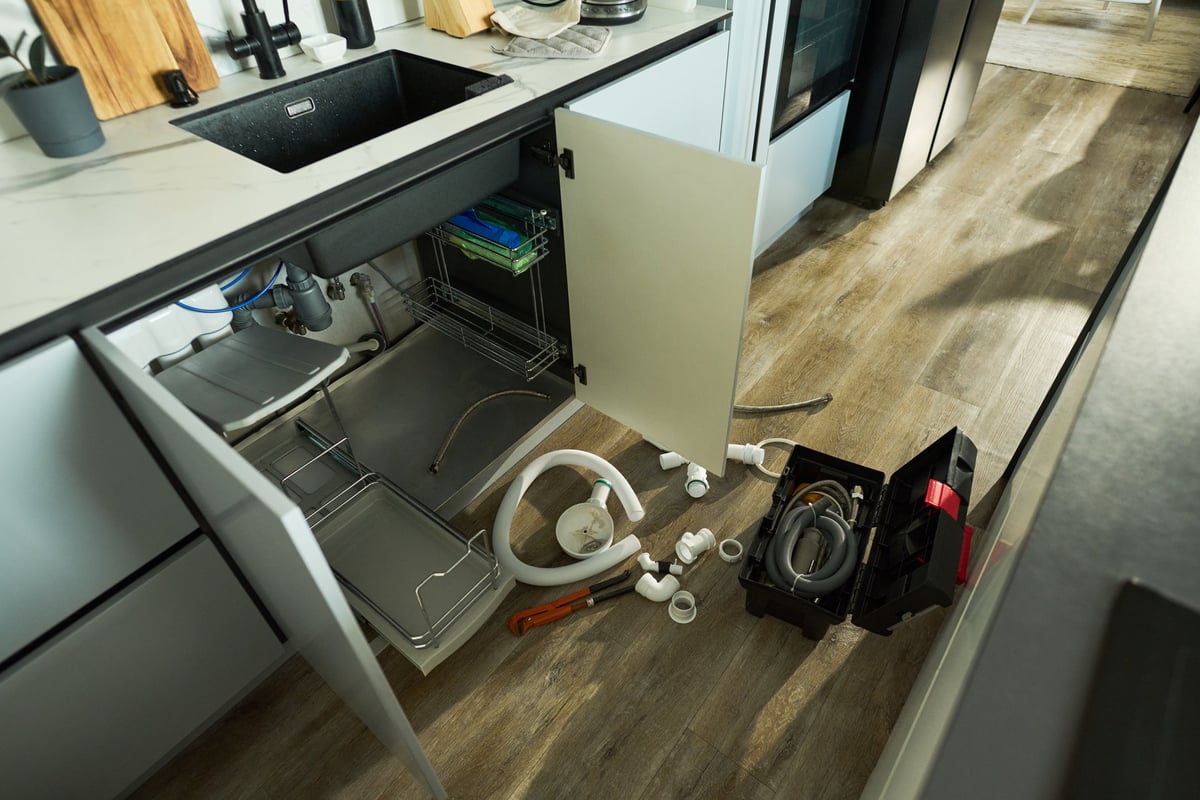 Open cabinet under a sink with plumbing tools and pipes during a repair