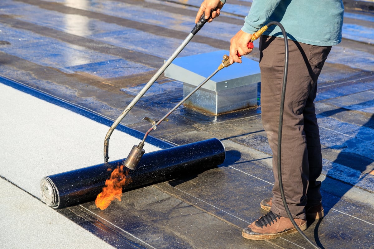 Roofer sealing a membrane layer on a flat roof with a torch